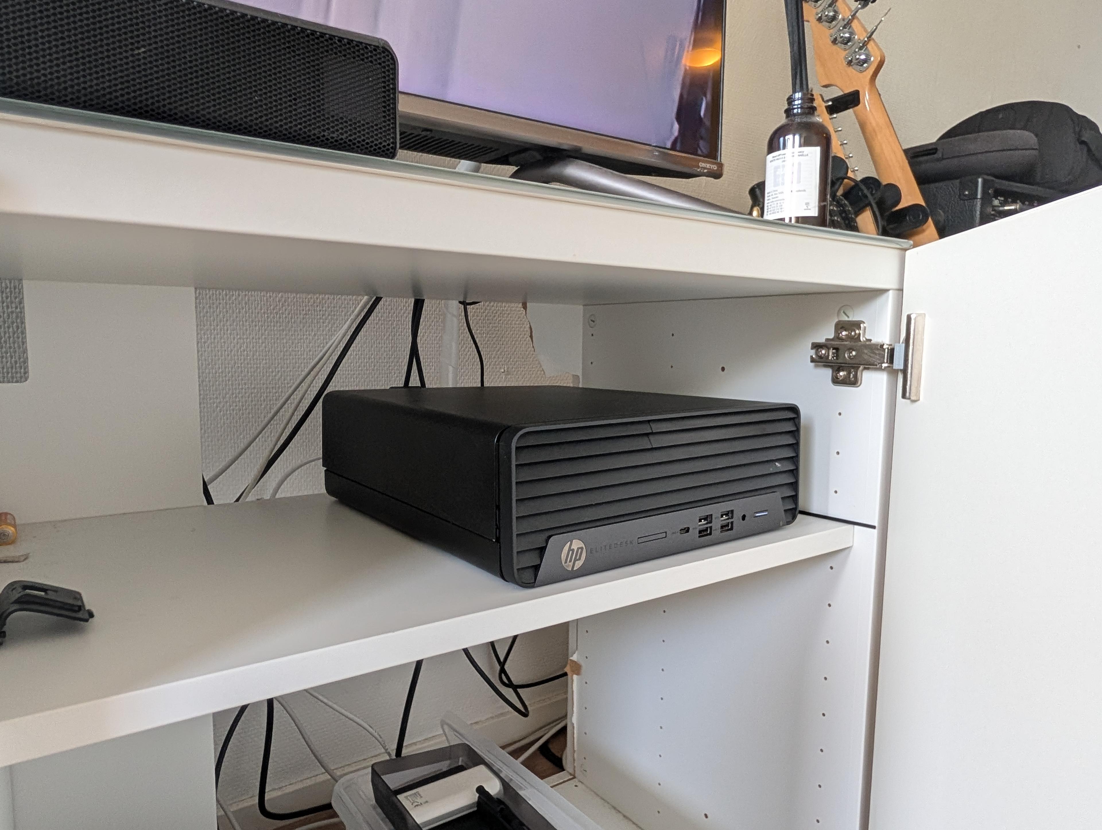Musta HP EliteDesk -tietokone avoimessa kaapissa television alla.
